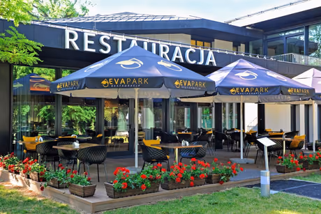 Wejście do restauracji EVA Park od strony parku, taras pod parasolami z szyldem RESTAURACJA