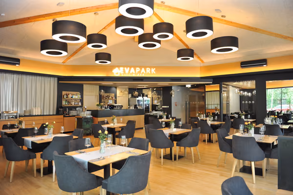 Sala główna restauracji z czarnymi lampami w kształcie walców, barem w głębi i jasną drewnianą podłogą