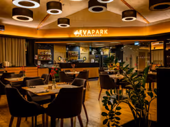 Sala restauracji wieczorem, ciepłe światło spod sufitu, czerwone goździki na stolikach