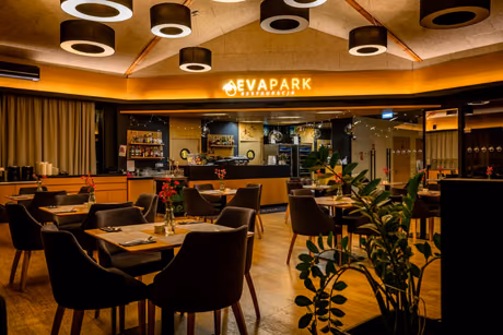 Sala restauracji EVA Park wieczorem, nakryte stoliki i podświetlony szyld